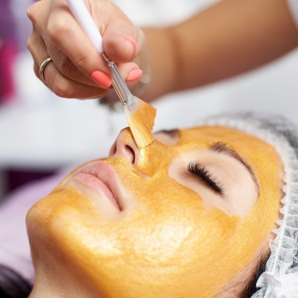 Macro photography of the hand of the beautician with the help of a special brush puts on the face of the girl a golden mask in the spa